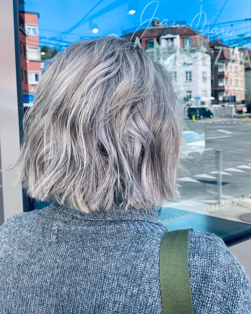 Kurzes, gewelltes Haar in natürlichem Grau mit hellen Strähnen